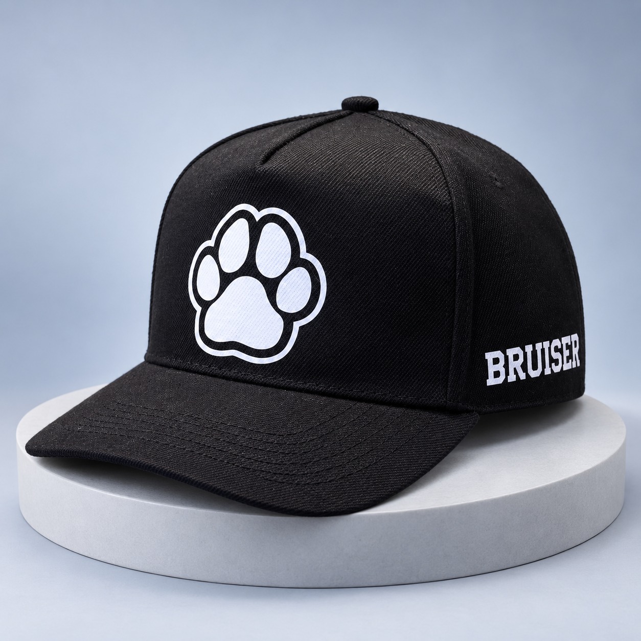 Black pup cap with a white paw on the front and BRUISER in white lettering on its side